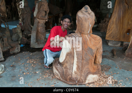 Un artisan sculpteur sur bois balinais à travailler sur une sculpture d'un grand Bouddha assis dans le village de Peliatan Banque D'Images