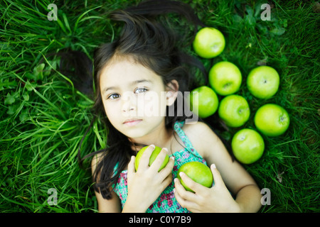 Fillette de six ans se trouve sur l'herbe avec des pommes vertes Banque D'Images