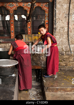 Deux jeunes moines bouddhistes bhoutanaises nettoyer la vaisselle du monastère après un délicieux repas dans un temple dans le centre de Bhoutan Banque D'Images