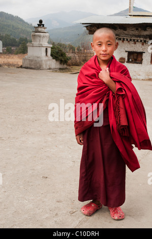 Jeune moine bouddhiste bhoutanais marche à travers les jardins du temple dans une robe marron sur sa façon d'exercer ses fonctions. Banque D'Images