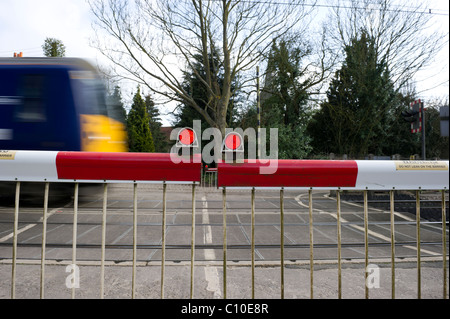 Train de voyageurs passant par un passage à niveau automatique. Obstacles et et voyant rouge montrant pour avertir le trafic. Banque D'Images