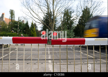 Train de voyageurs passant par un passage à niveau automatique. Obstacles et et voyant rouge montrant pour avertir le trafic. Banque D'Images