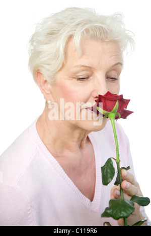 A mature woman smelling a le flétrissement rose rouge Banque D'Images