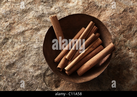 Bâtons de cannelle (Cinnamomum) dans un bol de cuivre sur une surface en pierre Banque D'Images