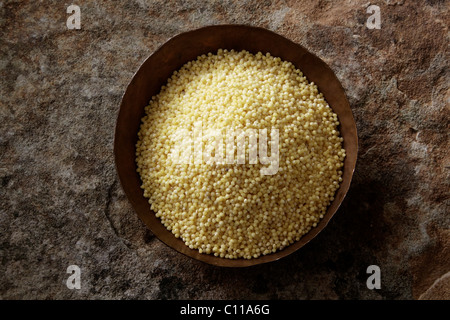 Millet (Panicum miliaceum) dans un bol de cuivre sur une surface en pierre Banque D'Images