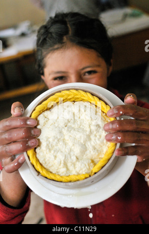 La production de fromage frais dans la vallée de Penas, rire jeune fille présente le fromage pressé en forme ronde, Oruro Banque D'Images