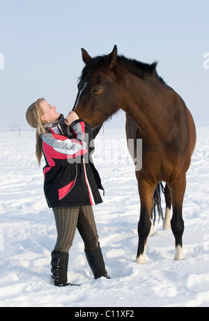 Fille, adolescent avec cheval brun sur un enclos couvert de neige Banque D'Images