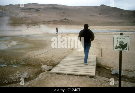 Un touriste sur une promenade passe un signe d'avertissement très chaud la masse à l'Namaskard solfatare champ dans le nord de l'Islande Banque D'Images