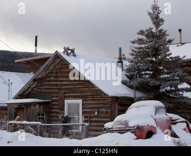 Vieille maison en bois et de vieux camions couverts de neige près du lac Bennett, Carcross, Territoire du Yukon, Canada Banque D'Images