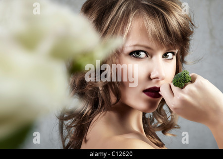 Portrait du côté d'une jeune femme tenant sa main avec un anneau de brocoli à seductively sa bouche, bijoux Banque D'Images