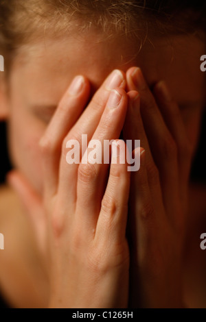 Young woman cachant son visage dans ses mains jointes Banque D'Images