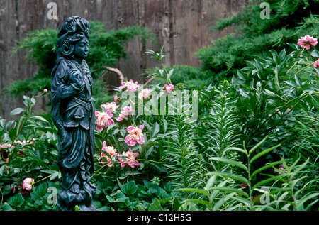 Statue en fonte asiatique apporte la grâce à une arrière-cour jardin adoucie par la violette, lys et de pivoines à la ligne de clôture, Midwest USA Banque D'Images