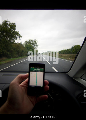 Un automobiliste roulant tout en utilisant un appareil mobile / téléphone mobile / téléphone intelligent. Pilote à l'aide de Google Maps / navigation Banque D'Images