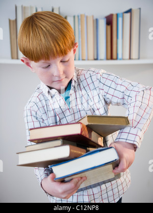 USA, New Jersey, Jersey City, Boy (8-9) transportant des livres empilés Banque D'Images
