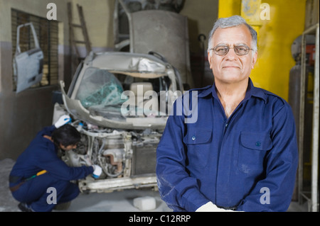 Portrait d'un mécanicien d'automobile avec un apprenti de la réparation d'une voiture à l'arrière-plan Banque D'Images
