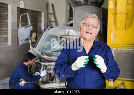 Portrait d'un mécanicien d'automobile avec un apprenti de la réparation d'une voiture à l'arrière-plan Banque D'Images