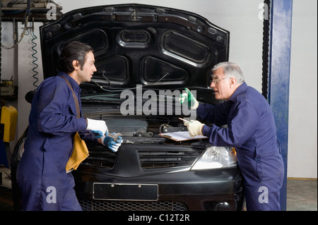 Avec un apprenti mécanicien auto réparation d'une voiture dans un garage Banque D'Images