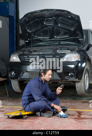 Mécanicien d'automobile à l'aide d'un téléphone mobile dans un garage Banque D'Images