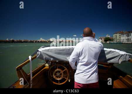 Un chauffeur/marin/pilote d'un bateau-taxi parle sur téléphone mobile tout en volant un taxi d'eau privé à Venise Italie Banque D'Images