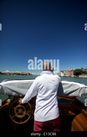 Un chauffeur/marin/pilote d'un bateau-taxi parle sur téléphone mobile tout en volant un taxi d'eau privé à Venise Italie Banque D'Images