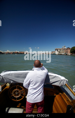 Un chauffeur/marin/pilote d'un bateau-taxi parle sur téléphone mobile tout en volant un taxi d'eau privé à Venise Italie Banque D'Images