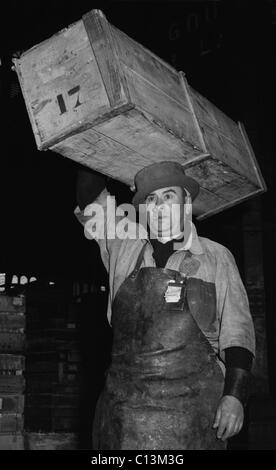 Porter, au marché central de Paris portant un chapeau spécial, étroit-, hard-hat couronné pour aider à équilibrer la caisse de poisson qu'il transporte sur sa tête. 1946. Banque D'Images