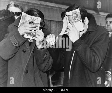 Deux étudiants de la ville de New York couvrant leurs visages avec des livres au siège de la police après qu'ils ont été ramassés sur les stupéfiants. 1968. Banque D'Images