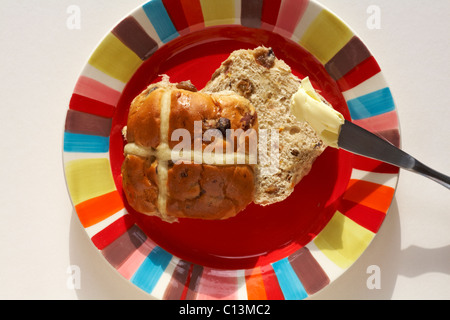 Hot cross bun tranché sur le point d'être sur la plaque beurrée rouge prêt pour Pâques sur fond blanc Banque D'Images