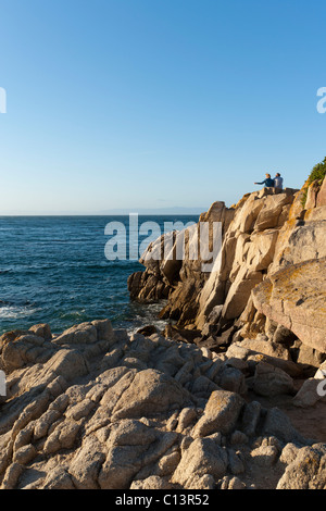 Des gens assis sur des rochers surplombant la baie de Monterey à Pacific Grove, Californie Banque D'Images