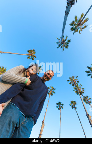 Couple hugging, looking at camera avec Sky et de palmiers derrière eux. Low angle POV. Santa Barbara, Californie, États-Unis Banque D'Images