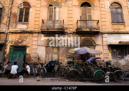 Un groupe de conducteurs de cyclo sont assis sur une rue ombragée à côté d'un immeuble délabré à Phnom Penh, Cambodge. Banque D'Images