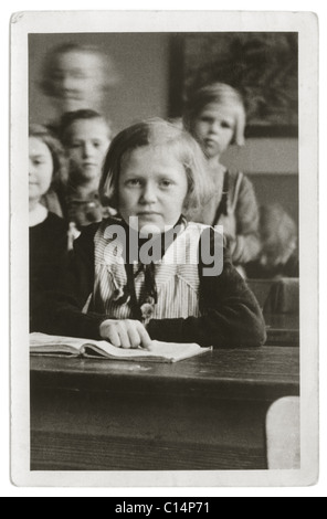 Lycéenne assise à son bureau avec un livre dans une classe de l'école primaire - 1930, U.K. Banque D'Images