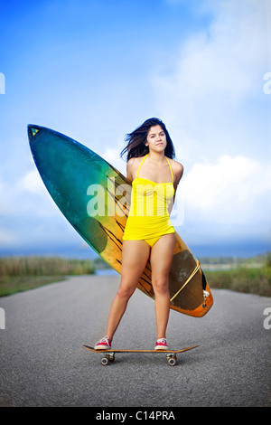 Jeune femme portant maillot jaune debout sur roulettes dans la route et la tenue de surf Banque D'Images