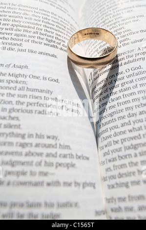 Un anneau de mariage jette une ombre sur les pages ouvertes d'un livre religieux Banque D'Images