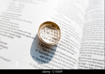 Un anneau de mariage jette une ombre sur les pages ouvertes d'un livre religieux Banque D'Images