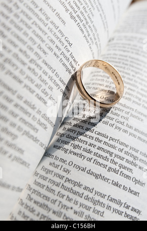 Un anneau de mariage jette une ombre sur les pages ouvertes d'un livre religieux Banque D'Images