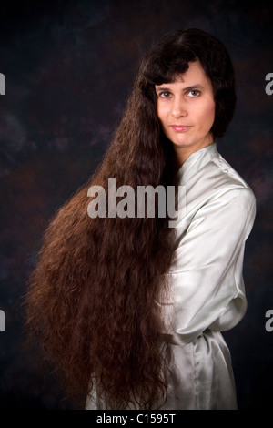 Aux cheveux extrêmement longs Middle Eastern woman dans une robe bleu clair pose devant un fond sombre. Banque D'Images