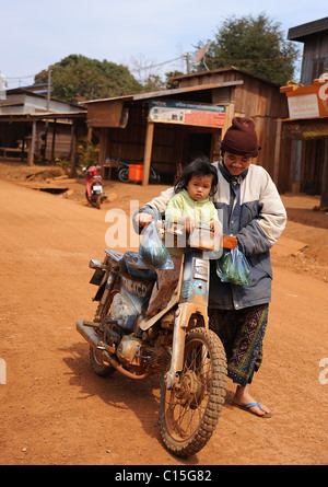 Femme poussant un jeune enfant sur une moto sur une route poussiéreuse de sable à Bousra Village, Mondulkiri, Cambodge Banque D'Images