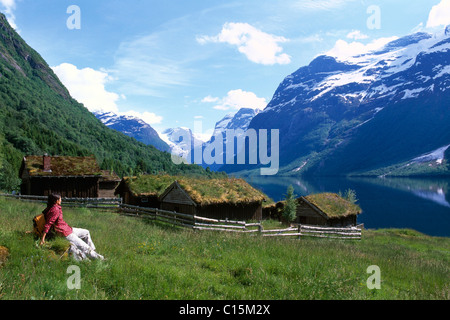 Femme assise en face de vieilles maisons sur les rives du lac Lovatnet, Loen, près du fjord de Nord, Norvège, Scandinavie, Europe Banque D'Images