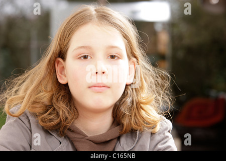 Garçon, 10 ans, avec de longs cheveux à la recherche dans l'appareil photo Banque D'Images