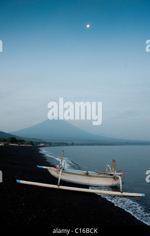 Avant le lever du soleil, un bateau de pêche traditionnel balinais, appelé un jukung, tire sur la plage avec Mt. Agung, dans l'arrière-plan. Banque D'Images