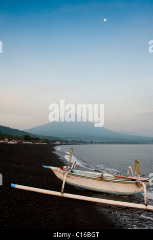 Avant le lever du soleil, un bateau de pêche traditionnel balinais, appelé un jukung, tire sur la plage avec Mt. Agung, dans l'arrière-plan. Banque D'Images