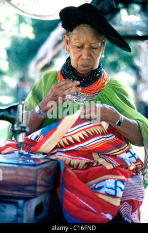 Une vieille femme indienne Miccosukee coud des vêtements traditionnels à l'extérieur à son Seminole village tribal dans les Everglades en Floride, USA. Banque D'Images