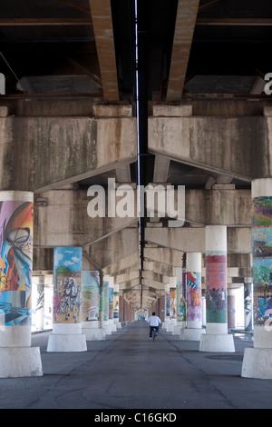 Man riding bicycle sous un viaduc de piliers décorés de peintures artistiques à La Nouvelle-Orléans Banque D'Images