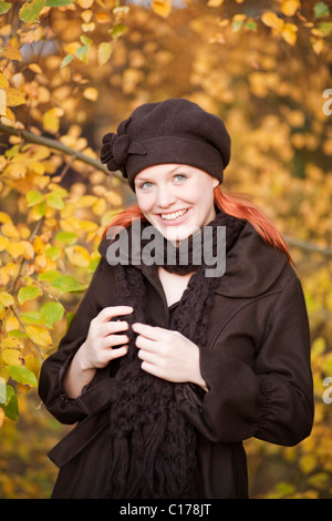 Jeune femme aux cheveux rouges portant un bonnet et écharpe en laine dans une forêt d'automne Banque D'Images