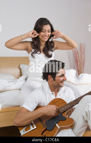 Un homme jouant de la guitare avec sa femme en mettant les doigts dans les oreilles Banque D'Images