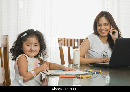 Fille d'une photo et sa mère à l'aide d'un ordinateur portable à côté d'elle à la table à manger Banque D'Images