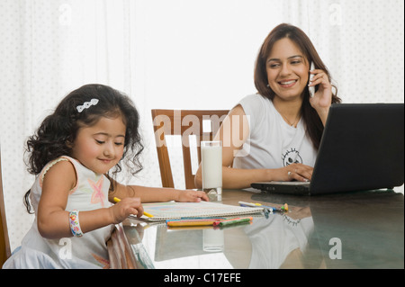 Fille d'une photo et sa mère à l'aide d'un ordinateur portable à côté d'elle à la table à manger Banque D'Images