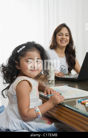 Fille d'une photo et sa mère à l'aide d'un ordinateur portable à côté d'elle à la table à manger Banque D'Images