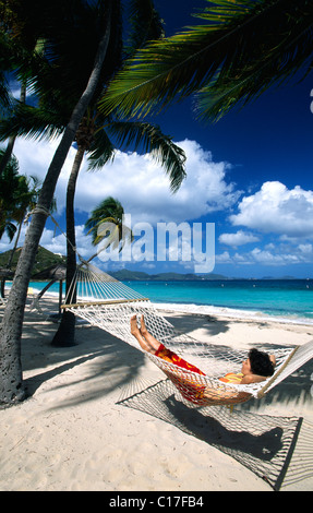 Femme dans un hamac sous les palmiers sur une plage sur Peter Island, British Virgin Islands, Caribbean Banque D'Images